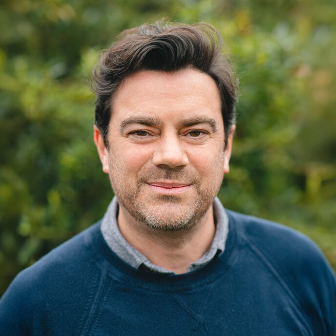 Simon Andrews, Managing Director at Retrofit West's portrait. Man with short brown hair, wearing a navy jumper. Blurred background.
