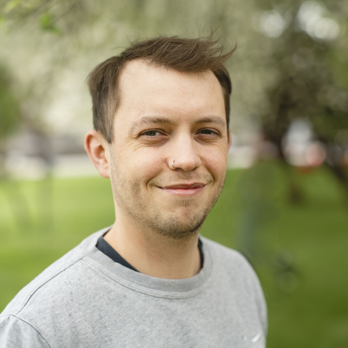 Portrait of man with brown hair wearing a grey jumper with a blurred background