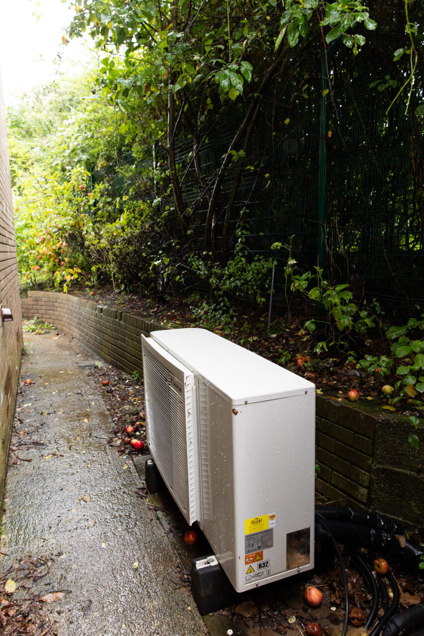 Photo showing an air source heat pump located in an alleyway at the side of a residential building