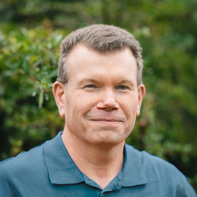 Portrait of Matt Williams. Man with short brown hair smiling at the camera wearing a dark blue polo.