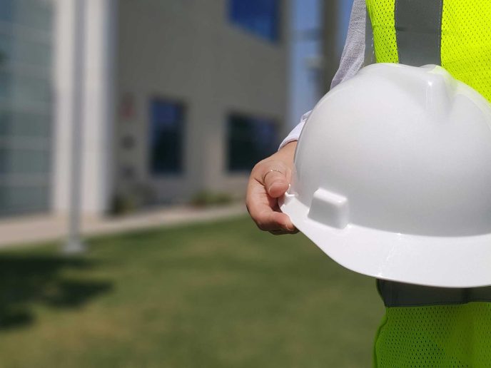 A closeup of someone in a hi-vis jacket holding a hard hat - Retrofit West Trusted Trades