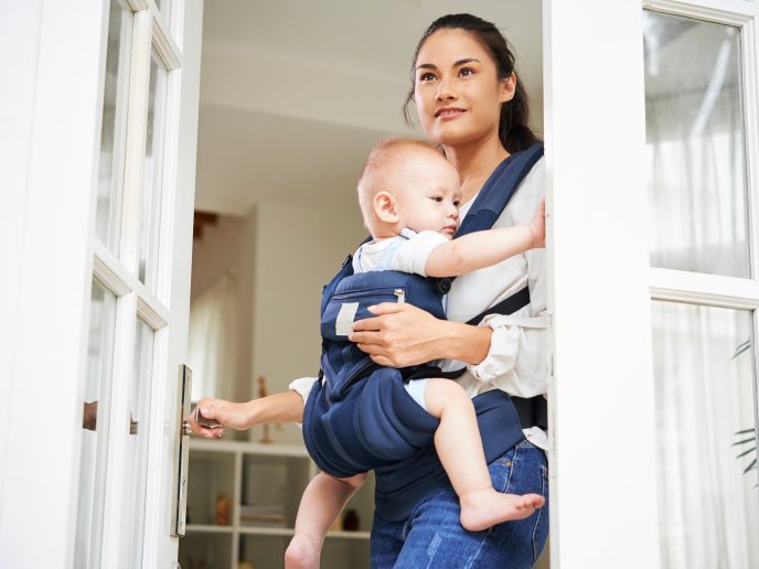 Pretty young mixed-race woman opening entrance door and leaving house with baby boy in carrier