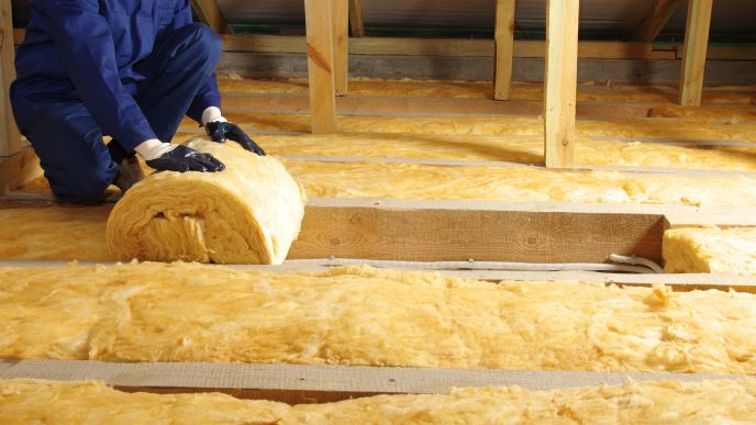 Worker thermally insulating house attic with glass wool