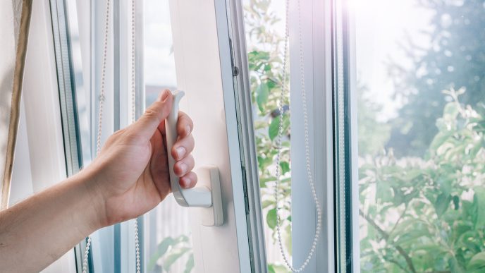 a hand opens a white, double-glazed PVC window