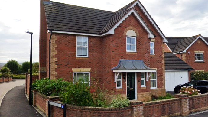 A red brick, detached home, about 30 years old with a front garden and garage.