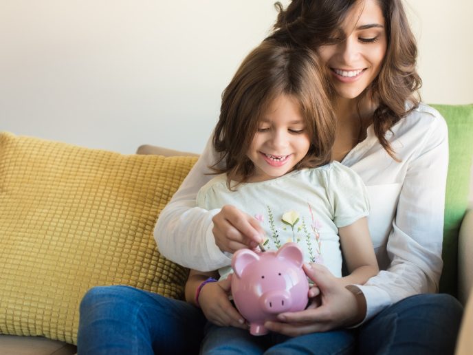 mother and young daughter put pennies in a piggbank