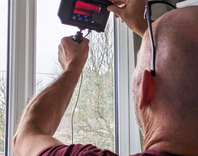 Man with thermal imaging camera examining the window for air leaks