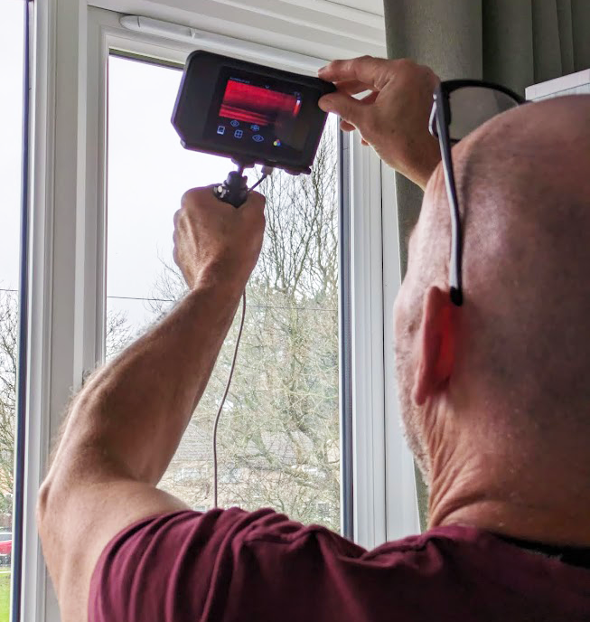 Man with thermal imaging camera examining the window for air leaks