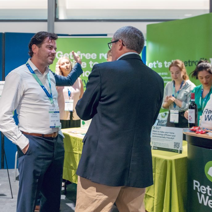 two men in suits talking with each other, stood in front of an exhibition stand