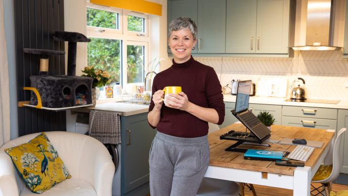 Smiling woman holding a hot drink in front of her light, clean kitchen