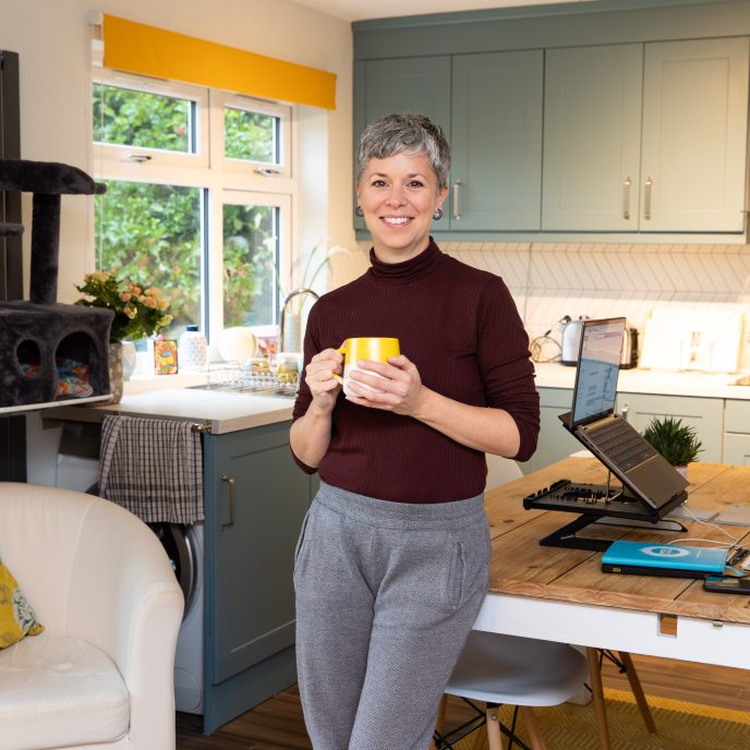 Smiling woman holding a hot drink in front of her light, clean kitchen
