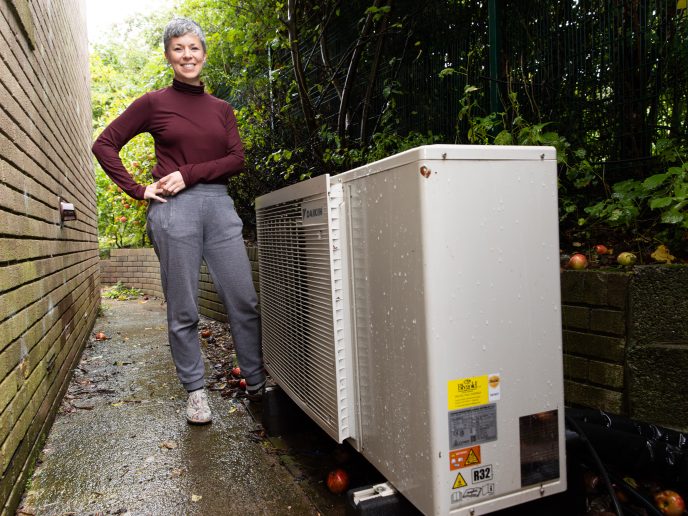 woman smiling, standing next to an air source heat pump outdoors