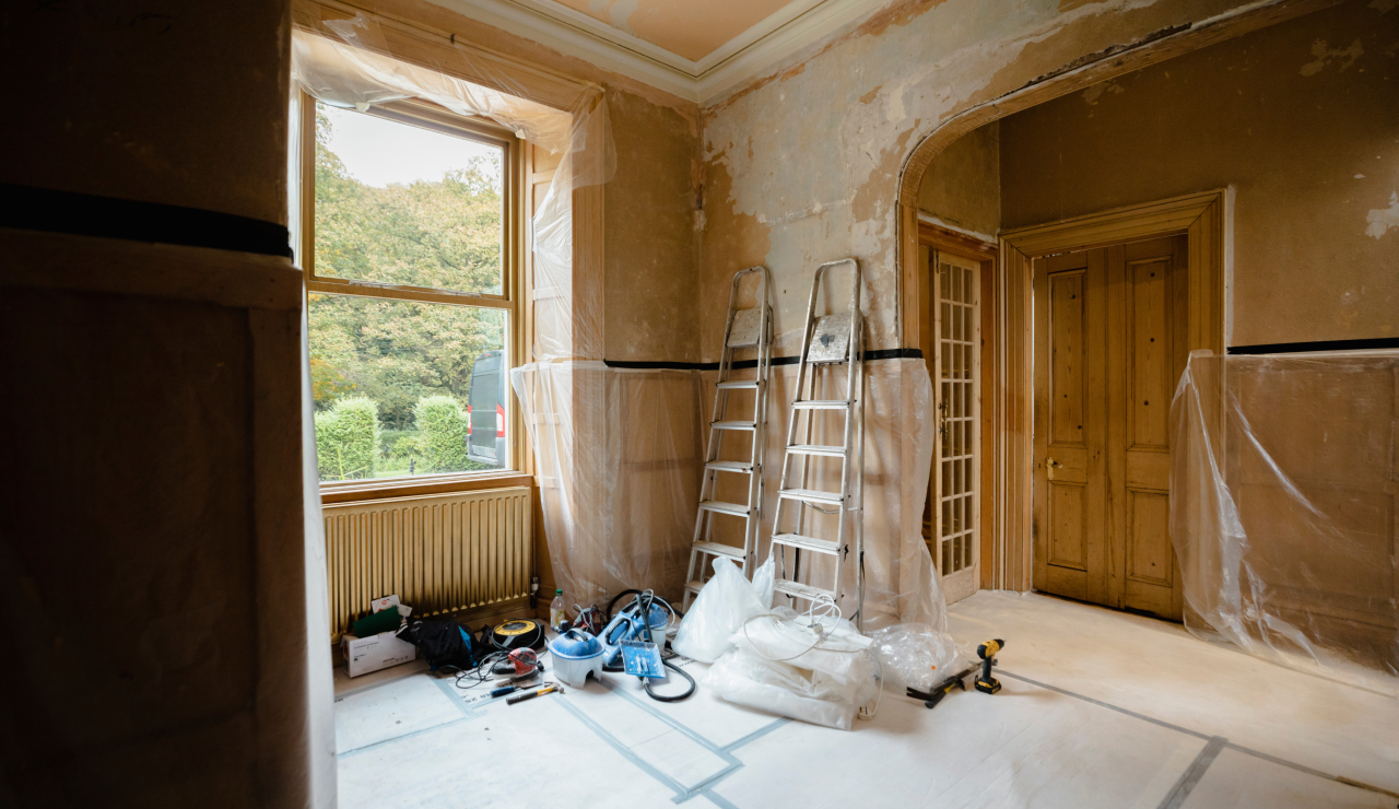 Room with ladders and other DIY equipment inside, plastic sheeting and stripped walls.