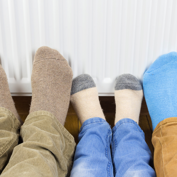 three sets of feet with socks on pressed to a radiator