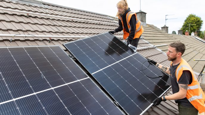 a man and a woman on the roof in hi-viz vests placing the solar panels on the installation rails.