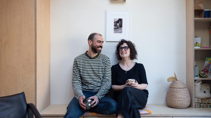 a laughing couple sat holding mugs on a minimalist wooden sideboard.