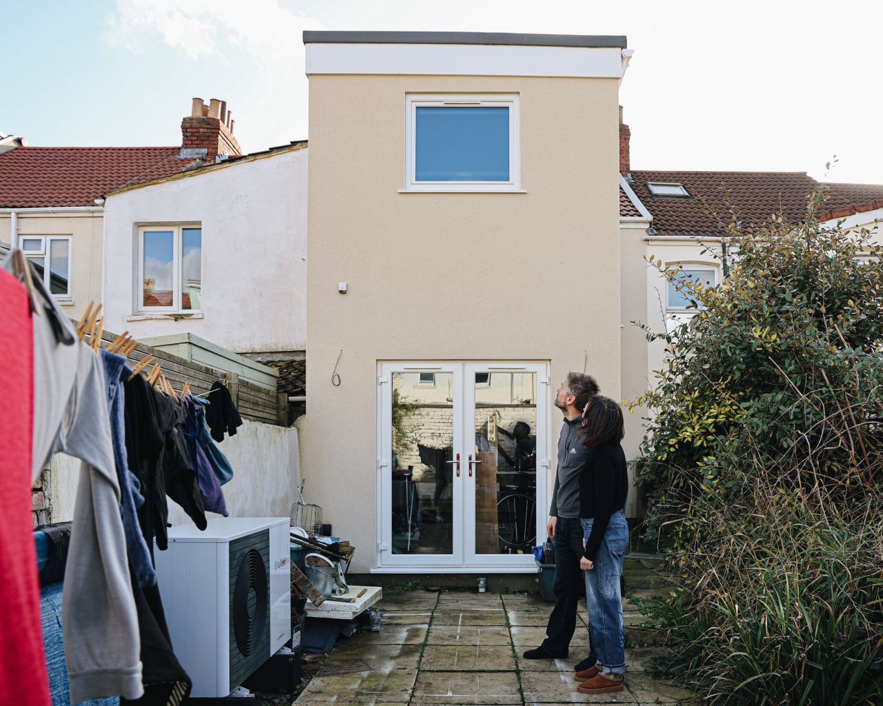 A man and a woman standing in their garden looking up at solar panels on the roof.