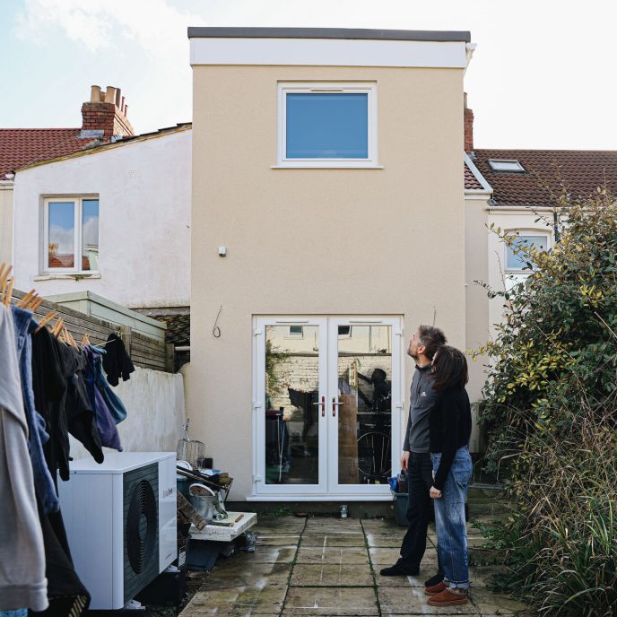 A man and a woman standing in their garden looking up at solar panels on the roof.