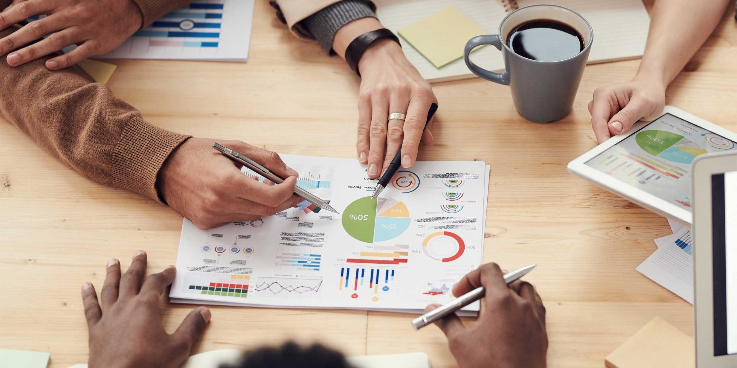 Table with printed graphs and multiple people sat around it discussing the metrics