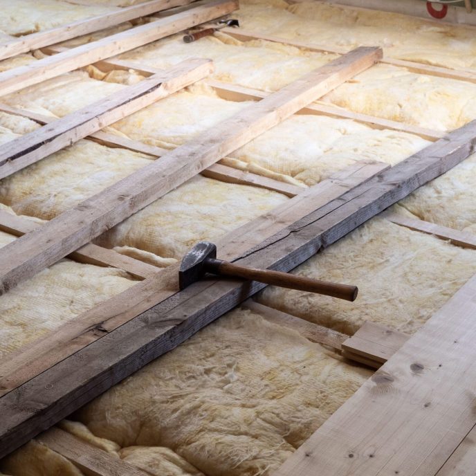 Laying wooden plank flooring on top of glass wool for warm insulation, with carpenter hammer