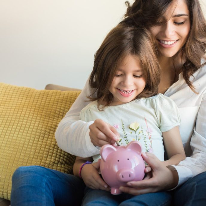 mother and young daughter put pennies in a piggbank