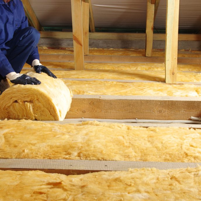 Worker thermally insulating house attic with glass wool