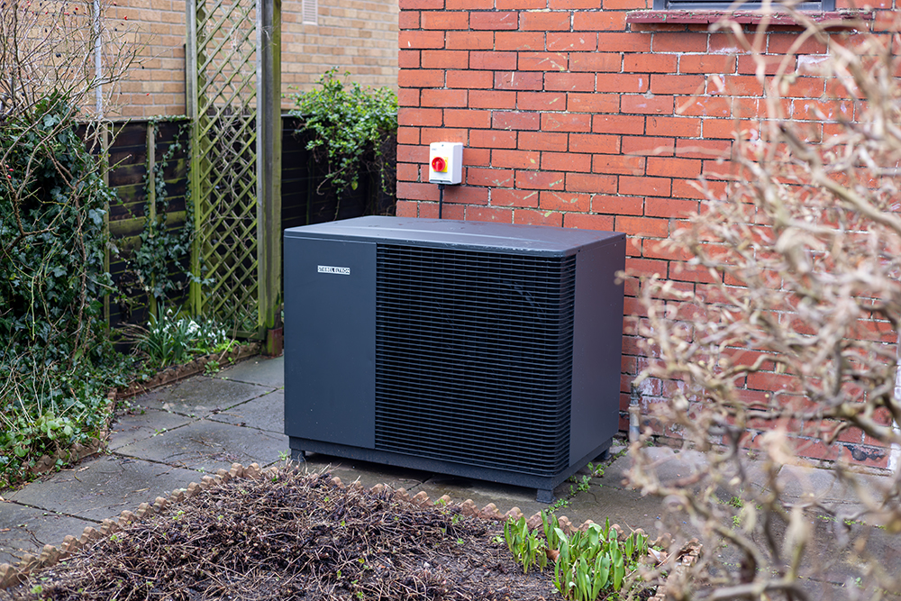 photo of sleep black heat pump in front garden with foliage around
