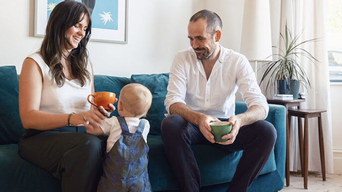 White female/ male couple drinking coffee with walking baby at their feet